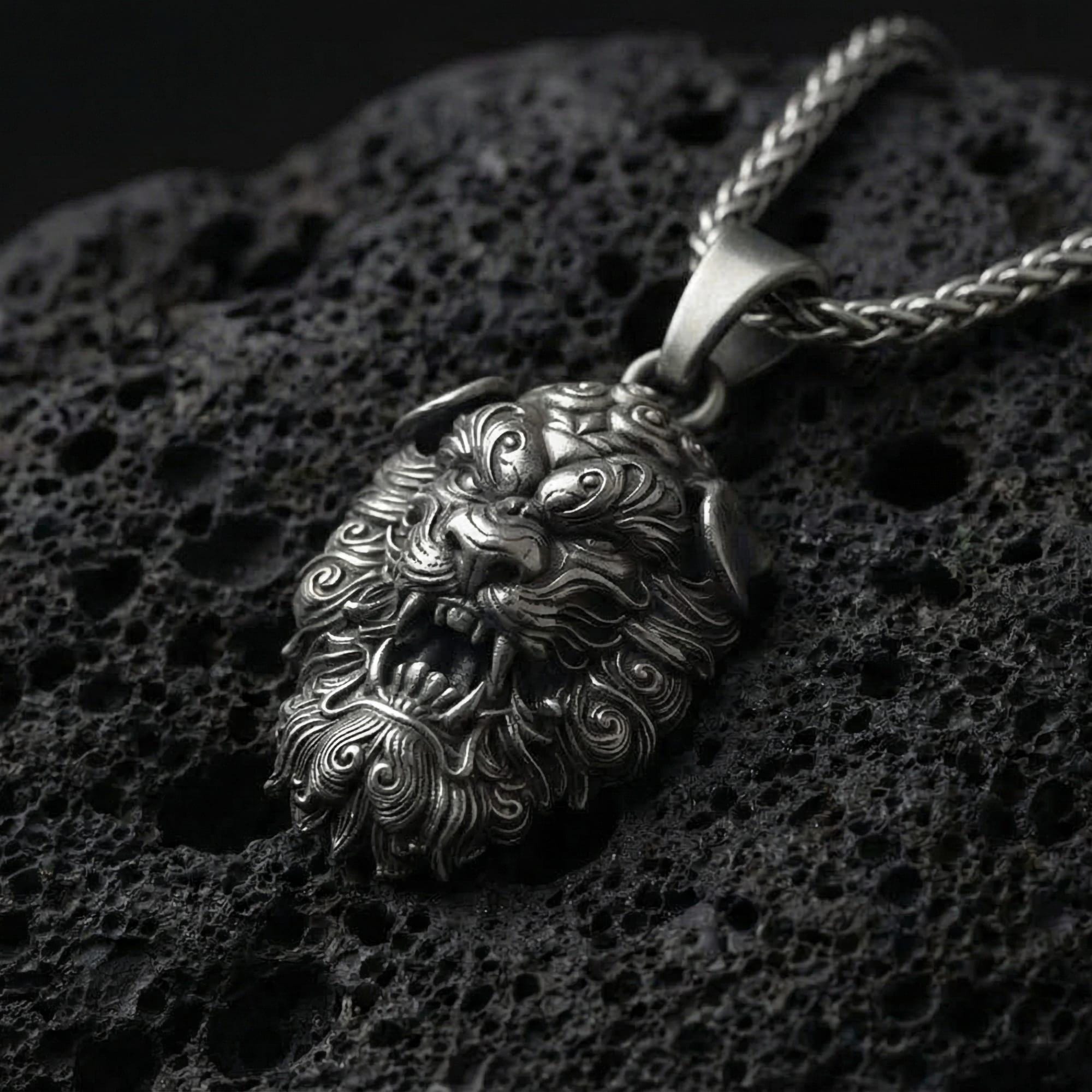 Oxidized Fu Dog pendant necklace photographed on volcanic rock with detailed Chinese guardian lion relief