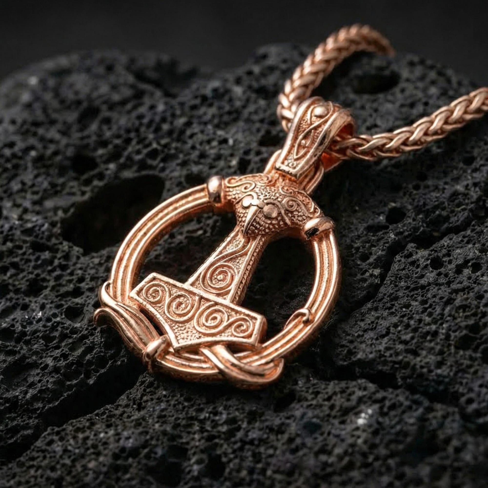 Rose gold plated Norse Mjölnir pendant necklace presented on volcanic rock surface with refined Viking myth aesthetic