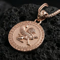 Load image into Gallery viewer, Rose gold plated winged lion pendant necklace photographed on volcanic rock with detailed mythical griffin style relief and Greek key border
