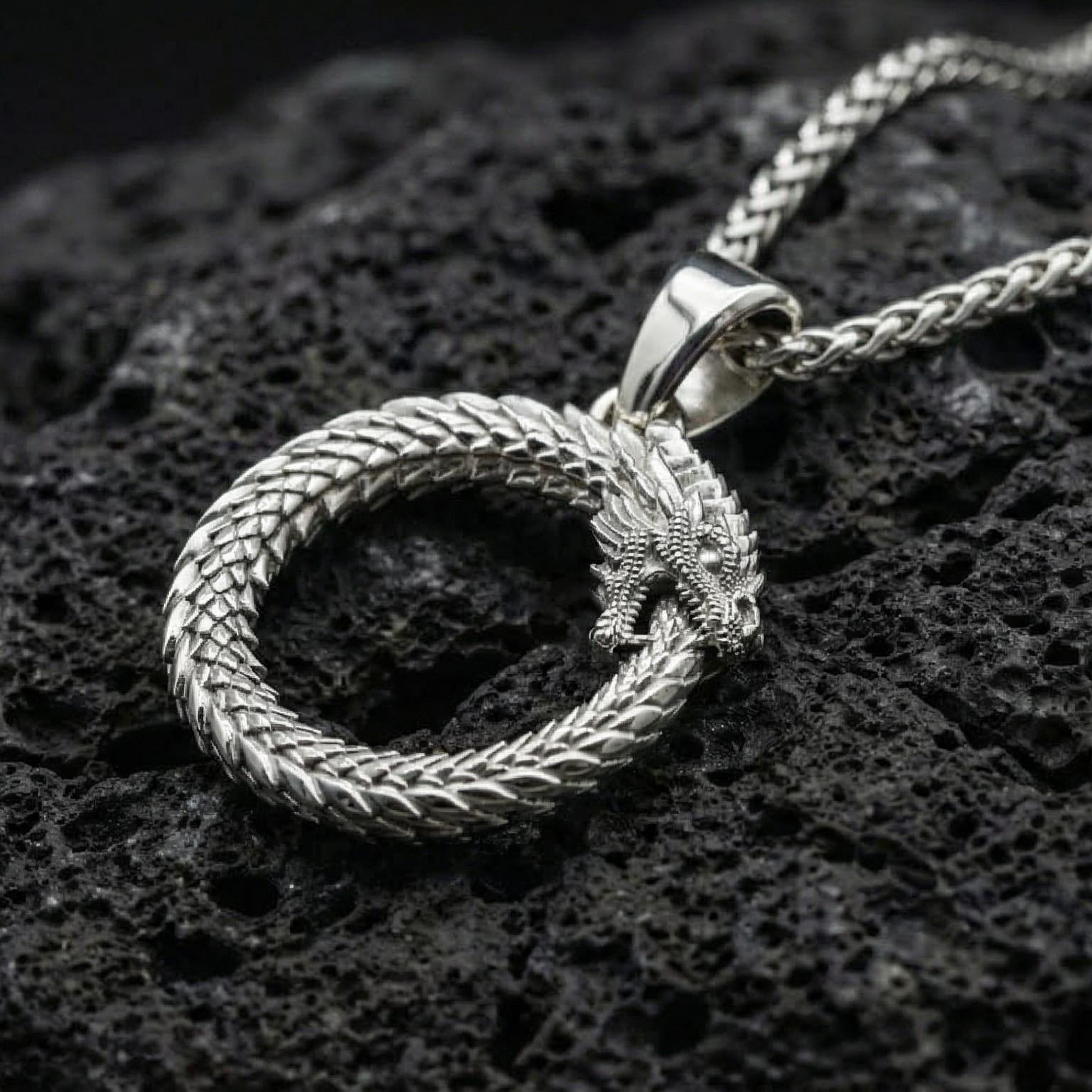 Polished silver ouroboros dragon serpent necklace displayed on volcanic stone background highlighting circular rebirth symbolism