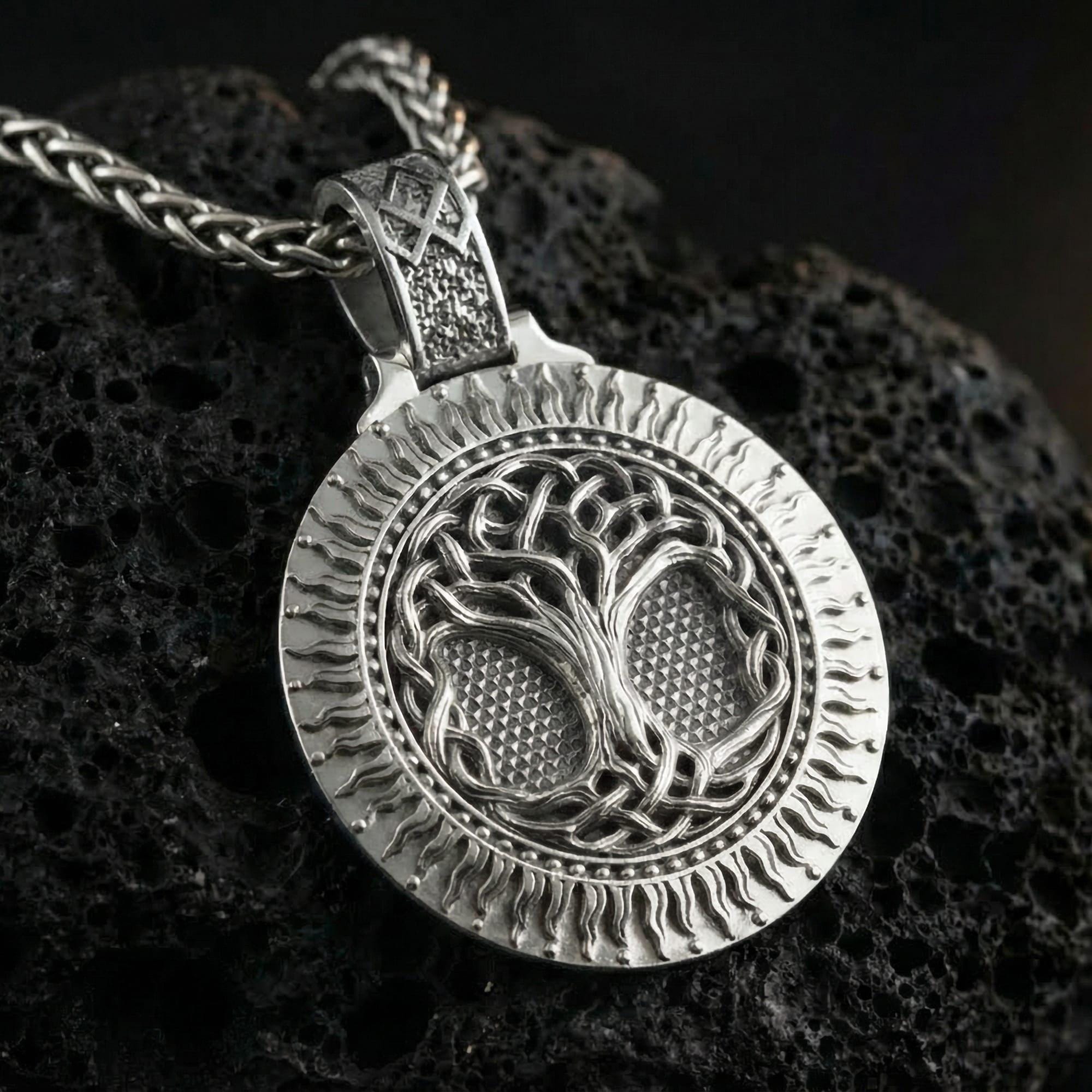 Polished silver Norse tree of life Yggdrasil pendant displayed on volcanic stone background with intricate circular relief