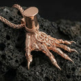 Load image into Gallery viewer, Rose gold plated Hand of Maliketh pendant necklace presented on volcanic rock surface with sinister fantasy aesthetic
