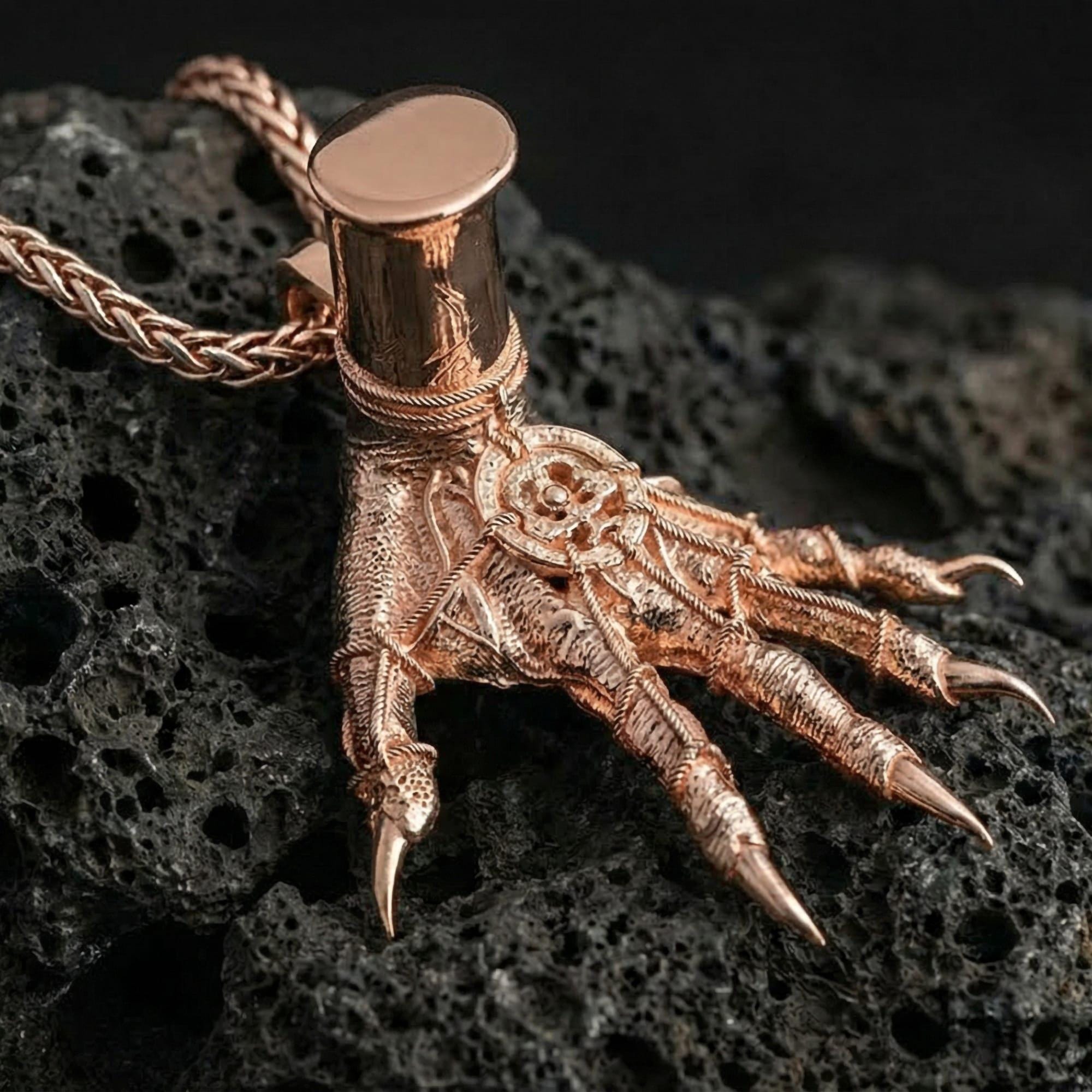 Rose gold plated Hand of Maliketh pendant necklace presented on volcanic rock surface with sinister fantasy aesthetic