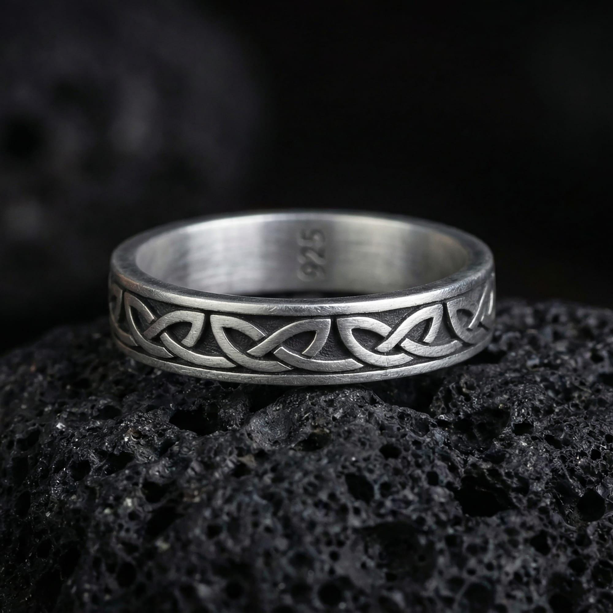 Oxidized Celtic knot ring photographed on volcanic rock with engraved endless knot pattern and dark oxidized contrast