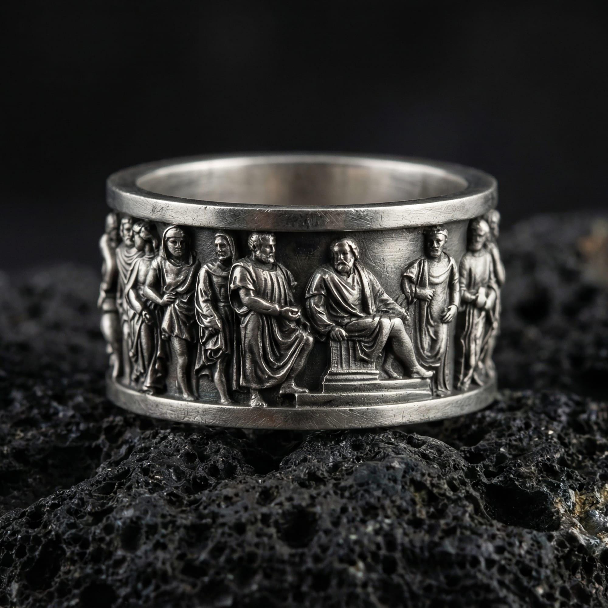 Oxidized ancient Greek philosopher band ring photographed on volcanic rock with high-relief classical figures and historical frieze detail