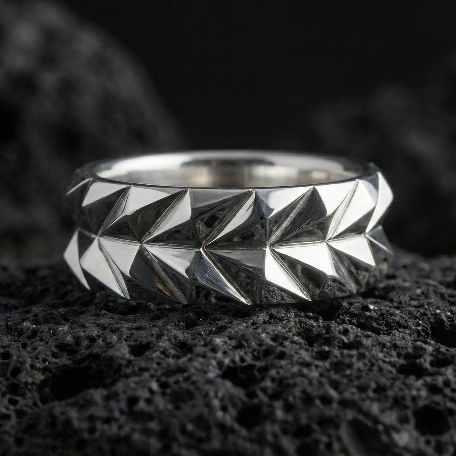 Polished silver faceted mens wedding band displayed on volcanic stone background highlighting precision-cut geometric surfaces and clean symmetry