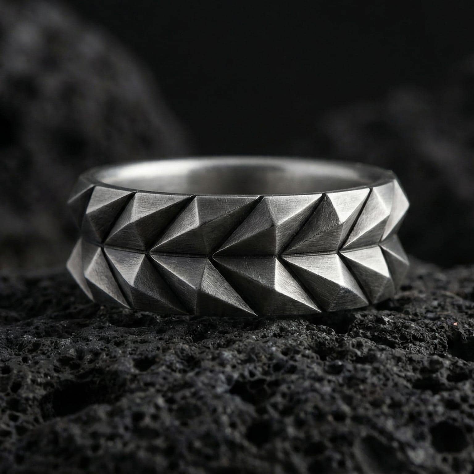 Oxidized geometric faceted silver band ring photographed on volcanic rock with sharp angular cuts and industrial modern texture