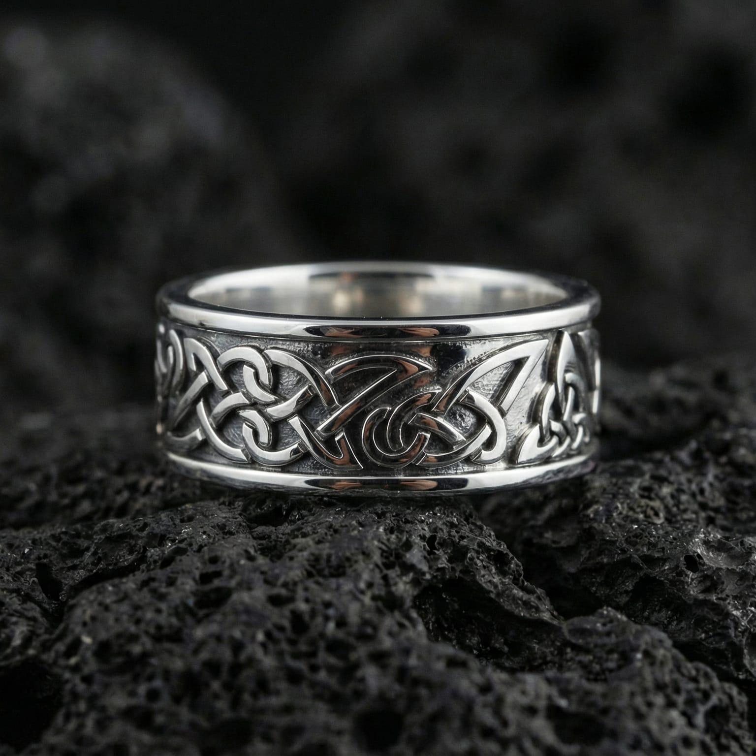 Polished silver Viking Celtic knot wedding band displayed on volcanic stone background highlighting clean edges and continuous infinity weave