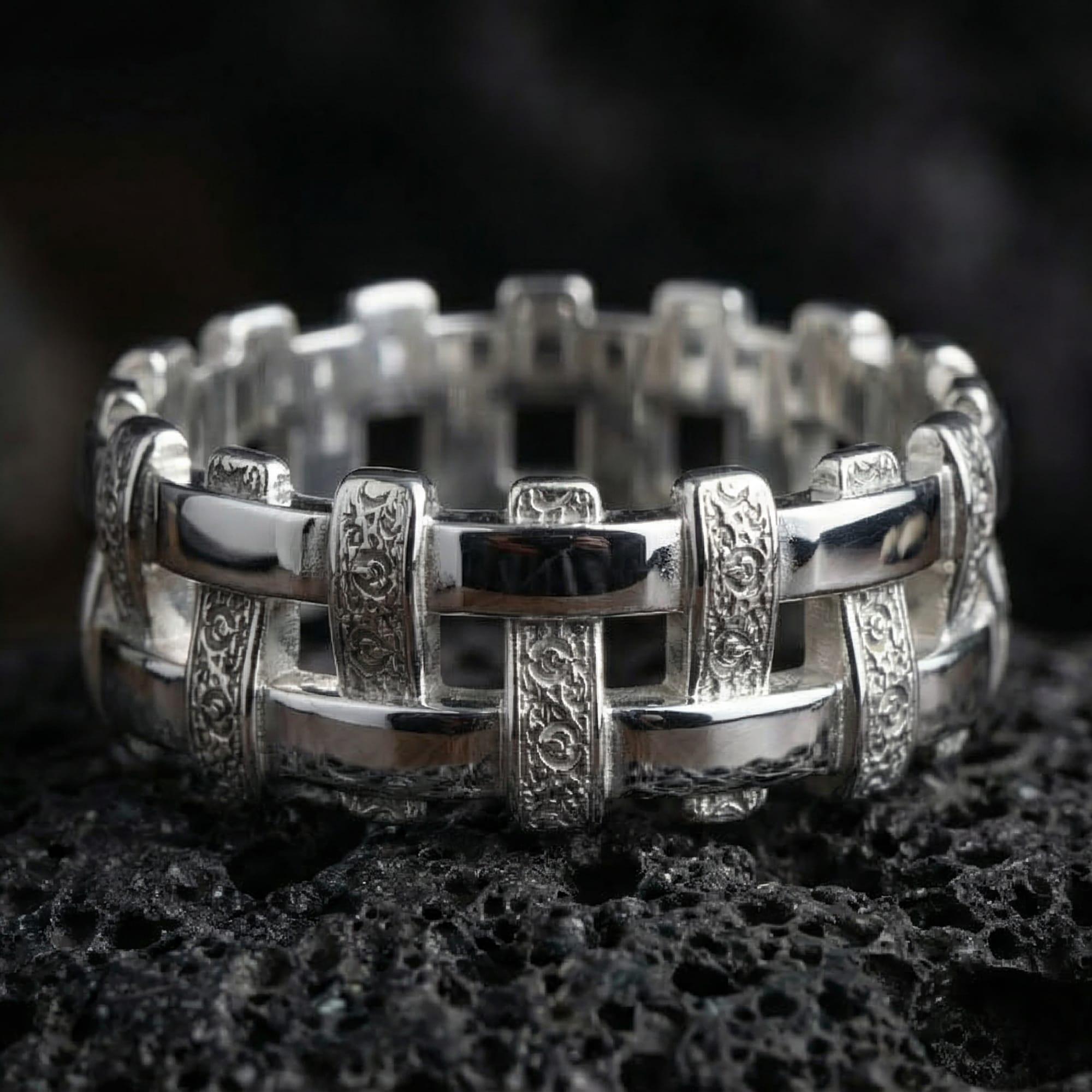 Polished silver woven pattern ring displayed on volcanic stone background highlighting raised cross-weave links and comfort fit