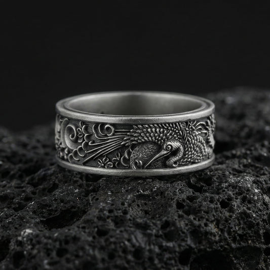Oxidized egret heron engraved band ring photographed on volcanic rock with detailed bird plumage relief and artisan nature motif carving