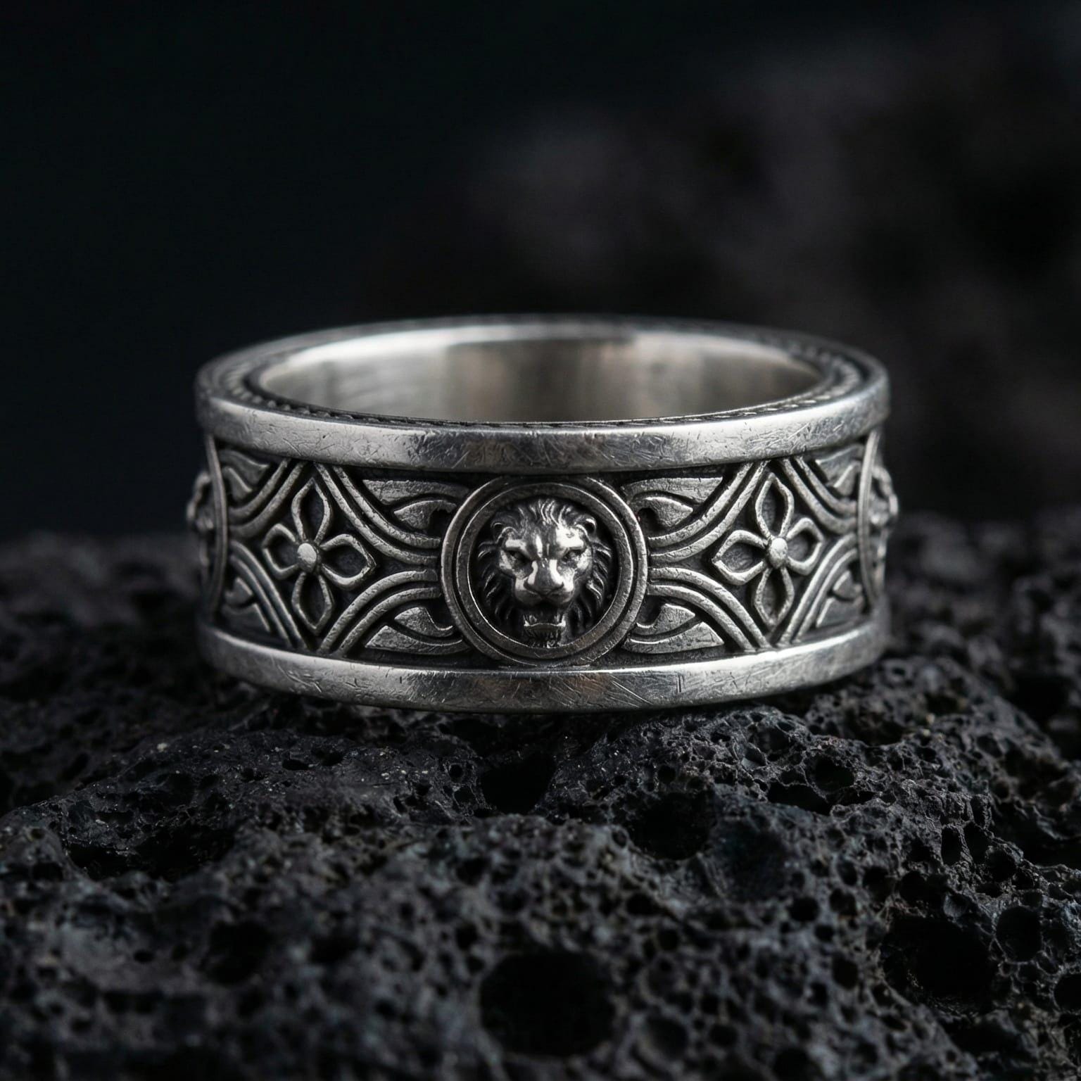 Oxidized lion head wedding band ring photographed on volcanic rock with raised feline crest centerpiece and medieval-inspired engraved details