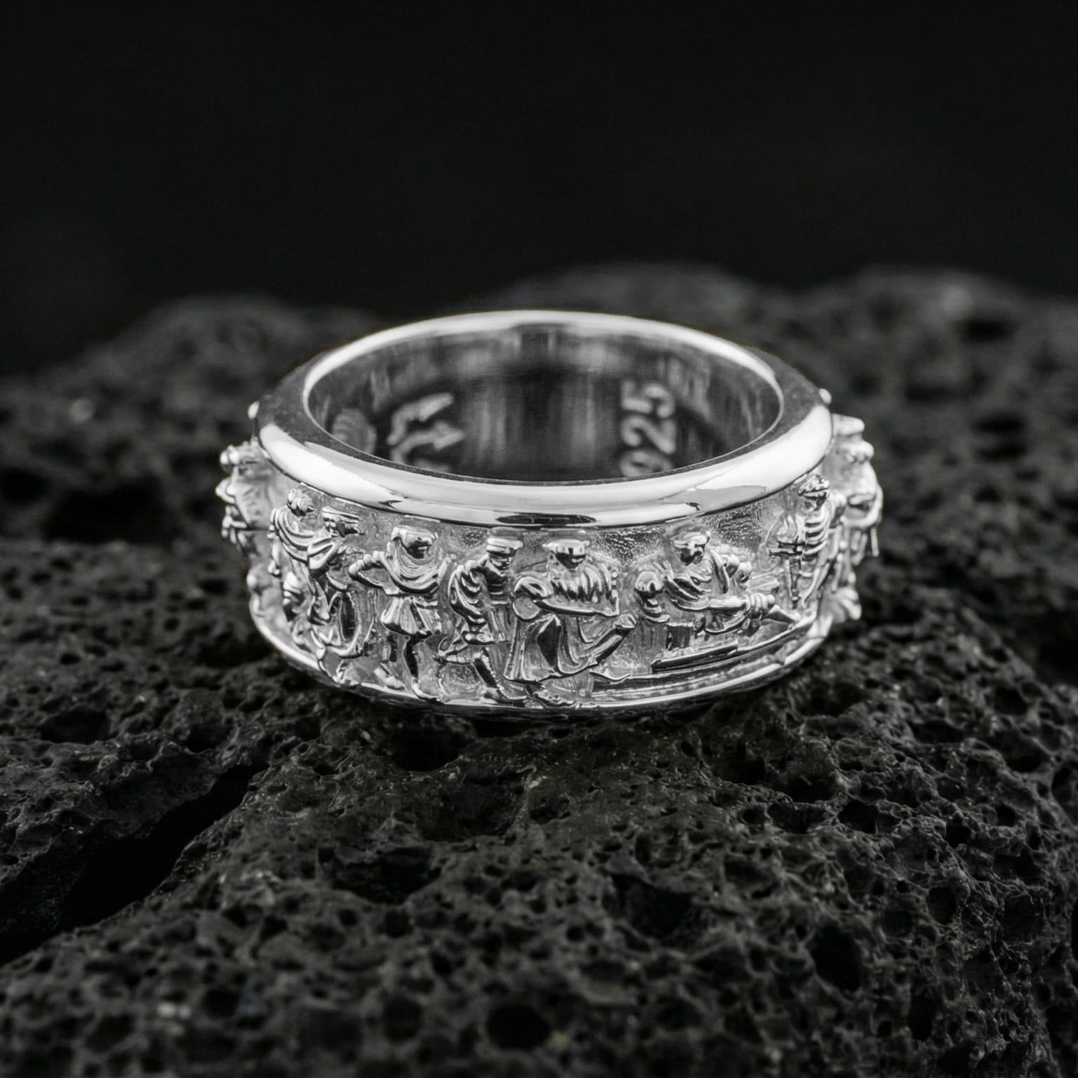 Polished silver rotating ancient Greek crowd wedding band on volcanic stone background highlighting crisp sculpted figures and depth