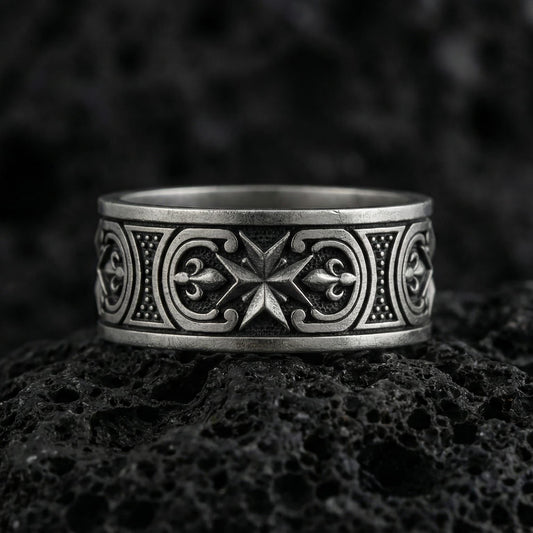 Oxidized Maltese cross Knights Hospitaller band ring photographed on volcanic rock, featuring crisp star-cross emblem and fleur de lis scrollwork detail