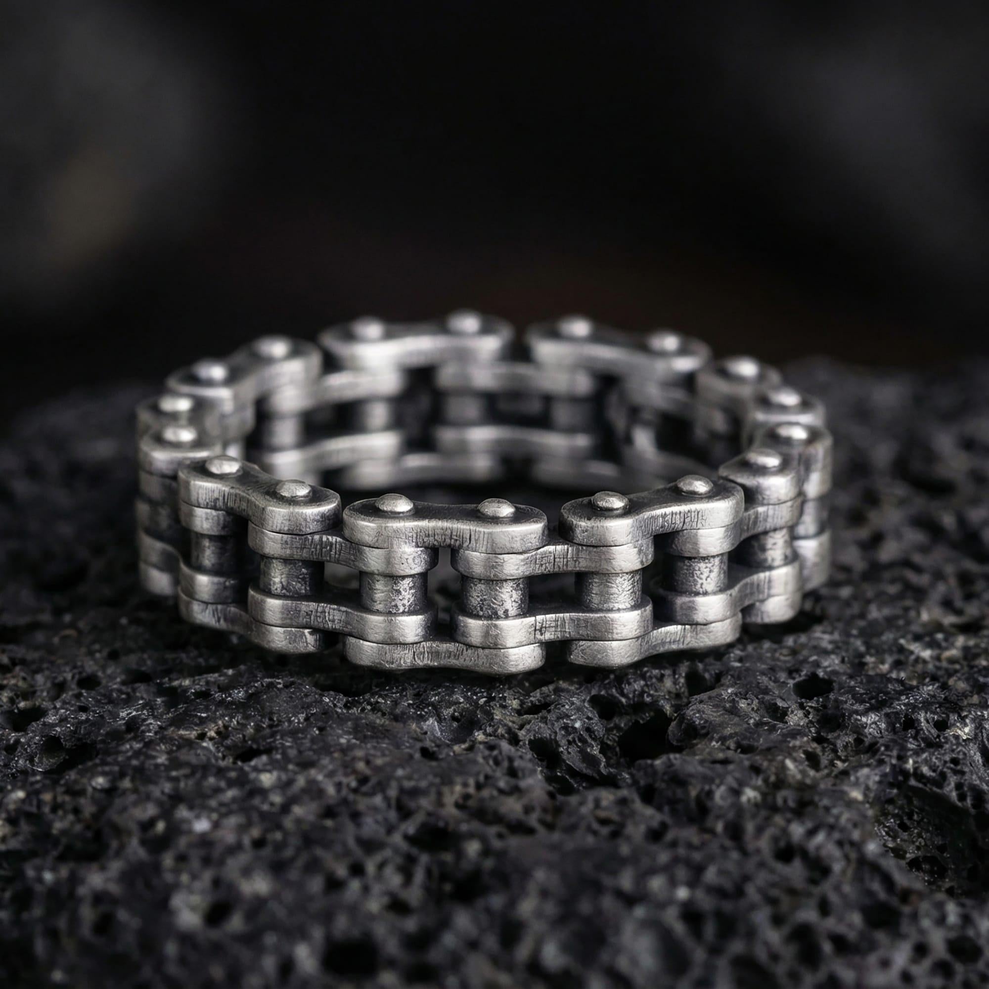 Oxidized steampunk chain link band ring photographed on volcanic rock, featuring industrial motorcycle chain texture and rugged mechanical detailing