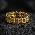 Load image into Gallery viewer, Gold plated retrofuturistic chain band ring showcased on volcanic rock, emphasizing bold gear-inspired styling and engineered symmetry
