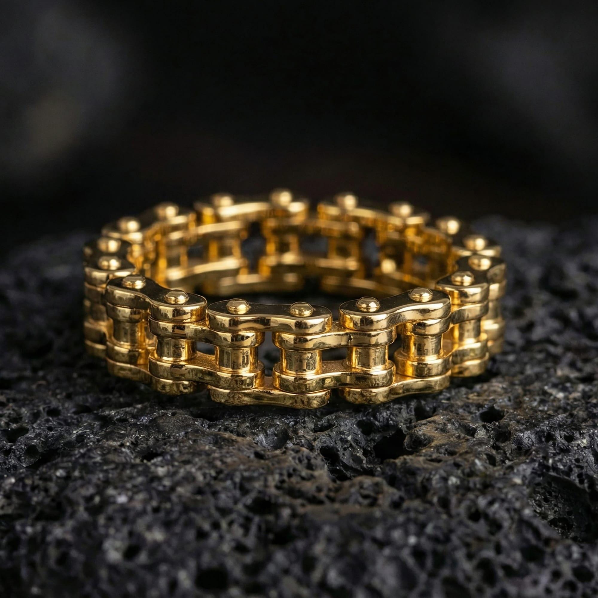 Gold plated retrofuturistic chain band ring showcased on volcanic rock, emphasizing bold gear-inspired styling and engineered symmetry