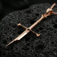 Load image into Gallery viewer, Rose gold plated sword jewelry pendant on volcanic rock, premium macro product photo, detailed hilt and blade profile

