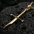 Load image into Gallery viewer, Gold plated sword pendant displayed on porous volcanic rock surface, close-up studio composition, refined metal shine
