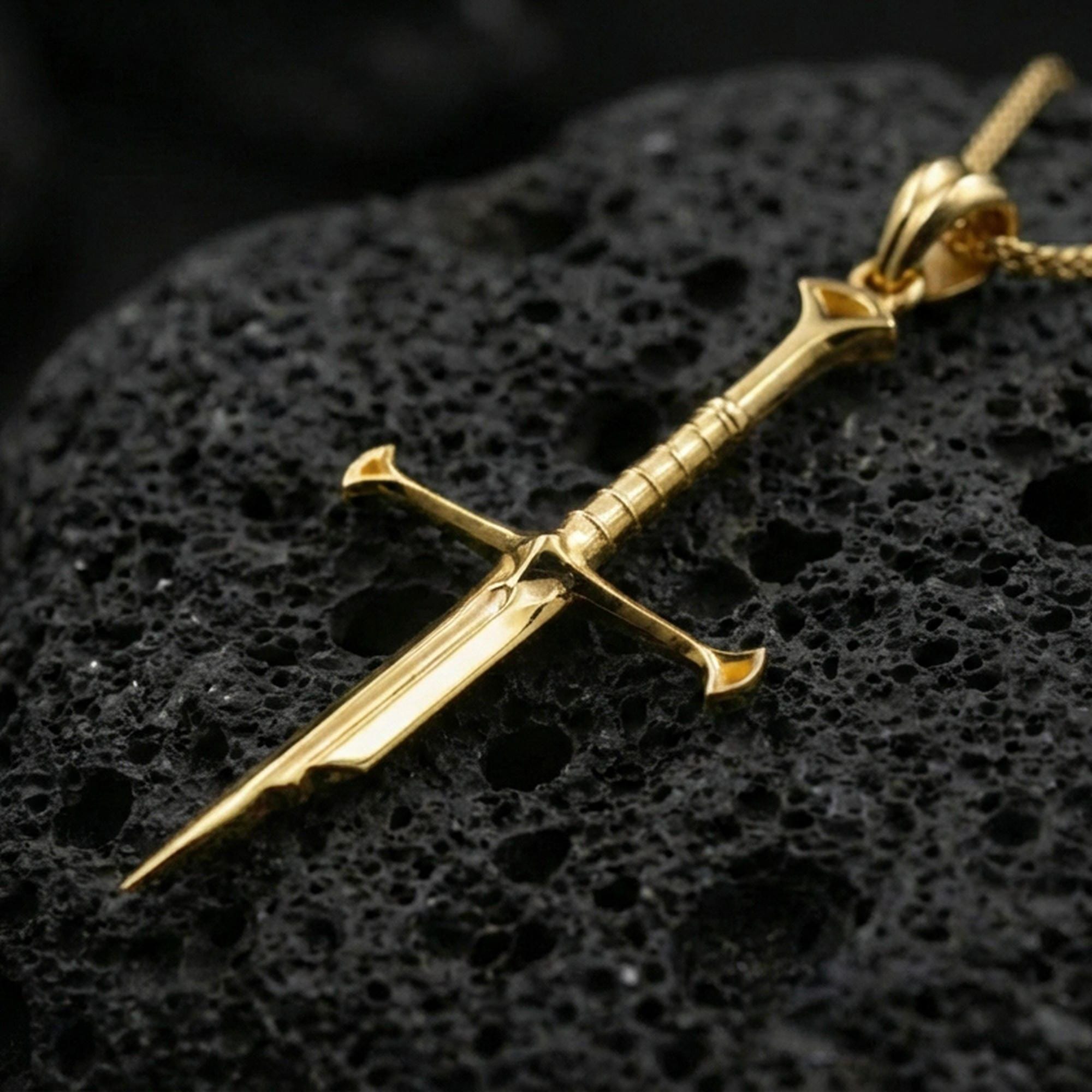 Gold plated sword pendant displayed on porous volcanic rock surface, close-up studio composition, refined metal shine