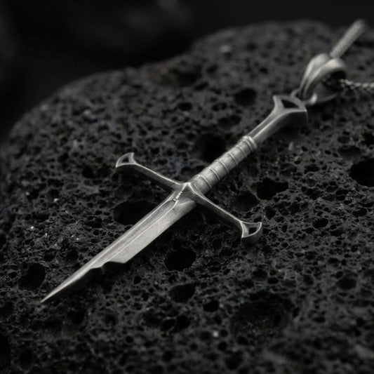 Oxidized sword pendant on textured volcanic rock, macro close-up, dark premium studio lighting, sharp blade detailing