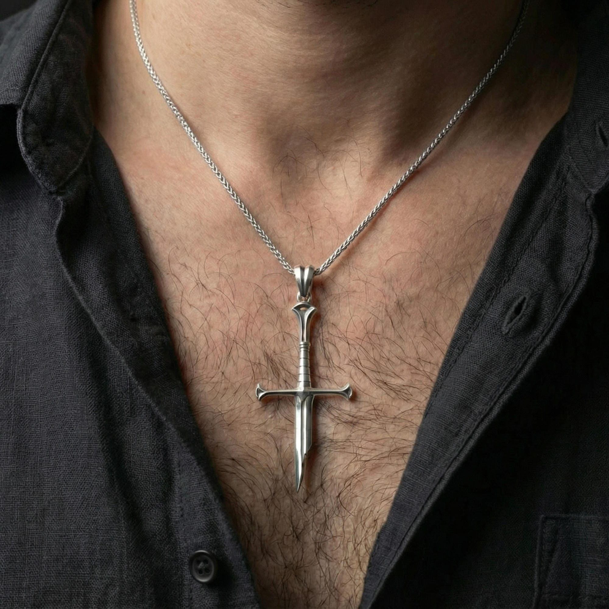 Polished silver sword pendant on chain worn on neck, natural lifestyle framing, blade and crossguard clearly visible