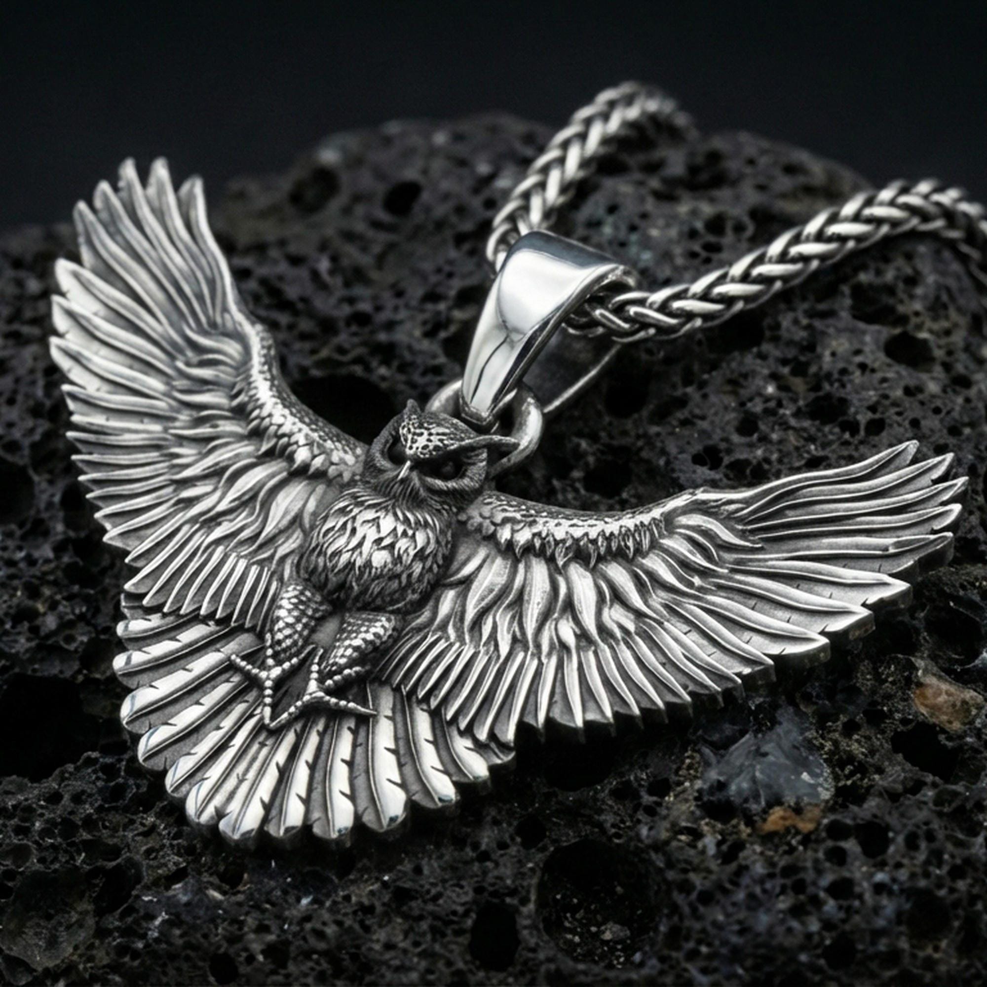 Polished silver owl necklace pendant on black volcanic stone background, crisp feather detailing, high-end product shot