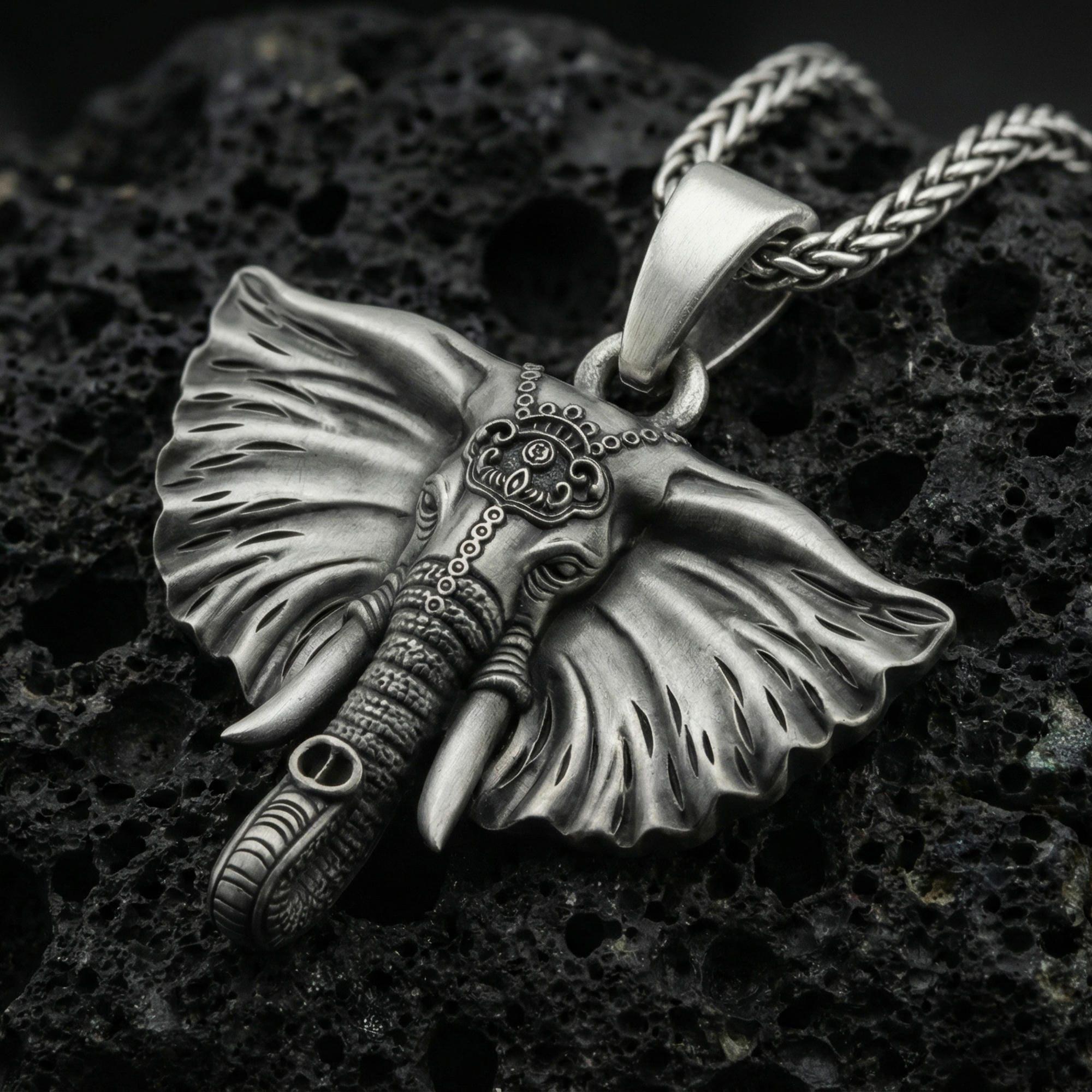 Oxidized elephant pendant on textured volcanic rock, macro close-up, detailed ears and tusks, dark premium studio lighting