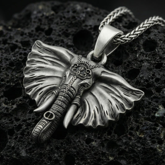 Oxidized elephant pendant on textured volcanic rock, macro close-up, detailed ears and tusks, dark premium studio lighting