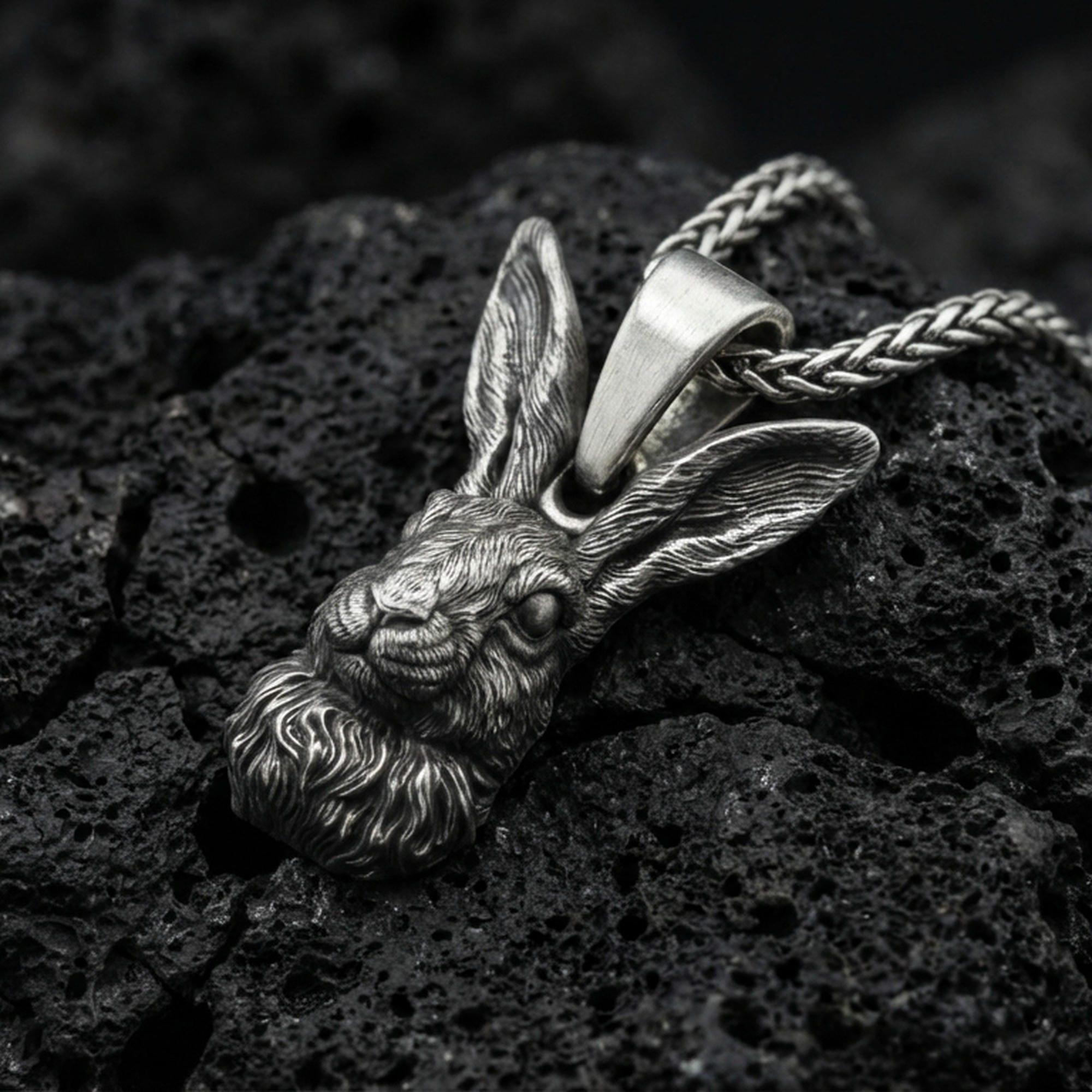 Oxidized rabbit head pendant on textured volcanic rock, macro close-up, detailed fur and ears, dark premium studio lighting