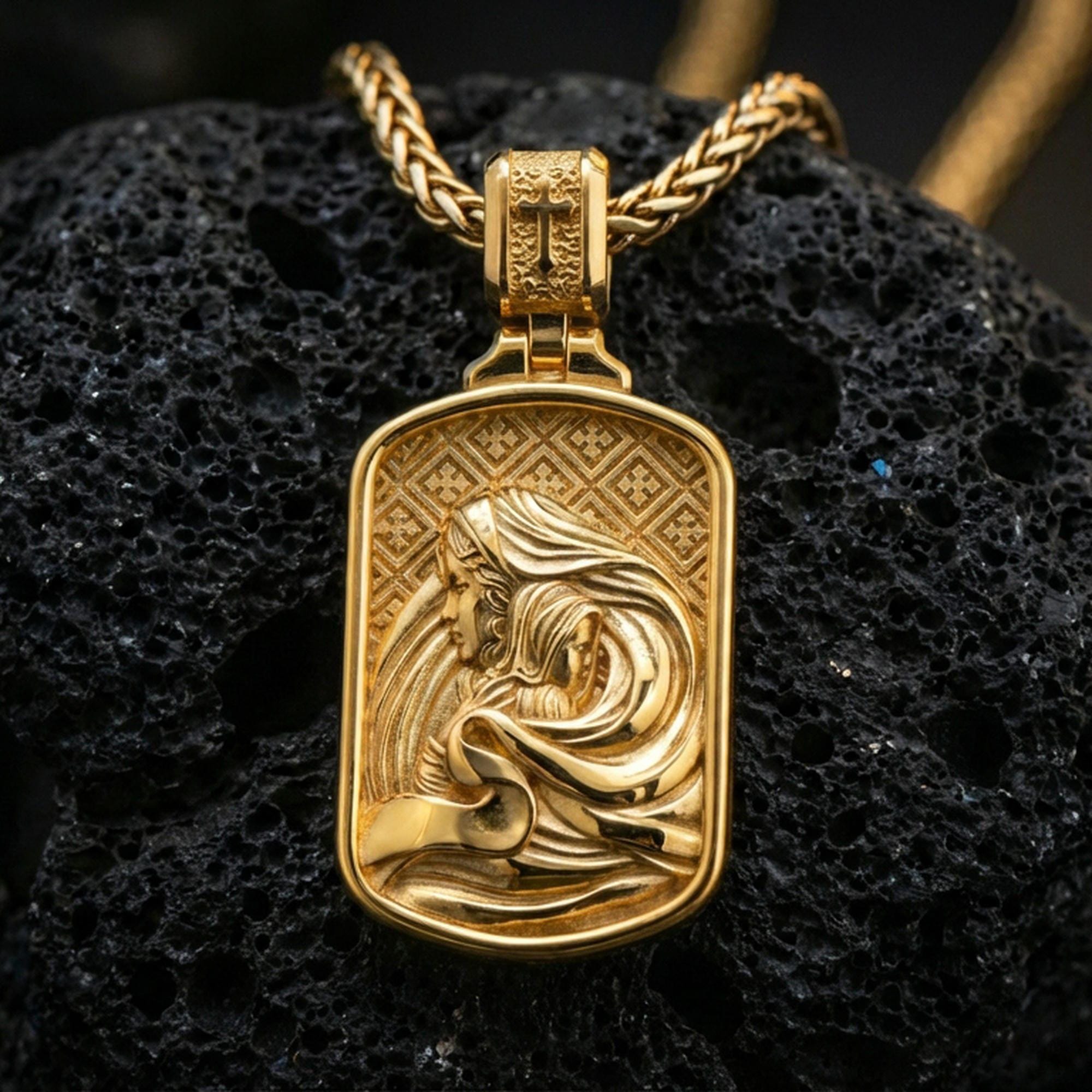 Gold plated Virgin Mary Baby Jesus pendant displayed on porous volcanic rock surface, close-up studio composition, detailed background pattern and bail