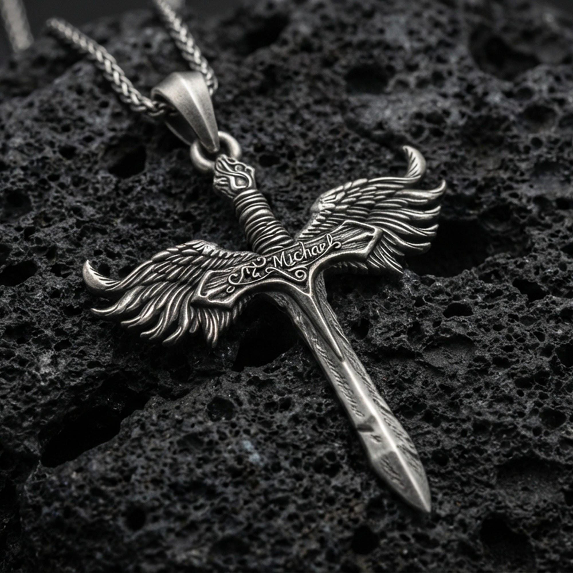 Oxidized Archangel Michael sword pendant on textured volcanic rock, macro close-up, winged crossguard detail, premium studio lighting