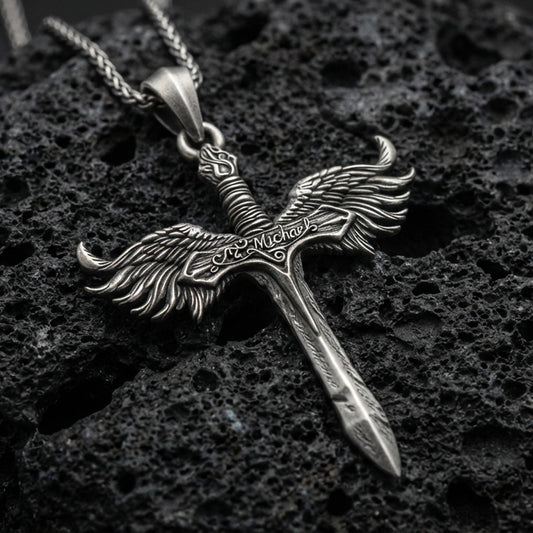 Oxidized Archangel Michael sword pendant on textured volcanic rock, macro close-up, winged crossguard detail, premium studio lighting