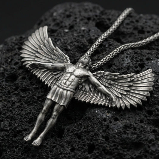 Oxidized Archangel Michael pendant on textured volcanic rock, macro close-up, full-body angel figure with spread wings, premium studio lighting