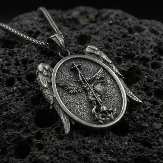 Oxidized Saint Michael archangel pendant on textured volcanic rock, macro close-up, oval medallion with wing accents, premium studio lighting