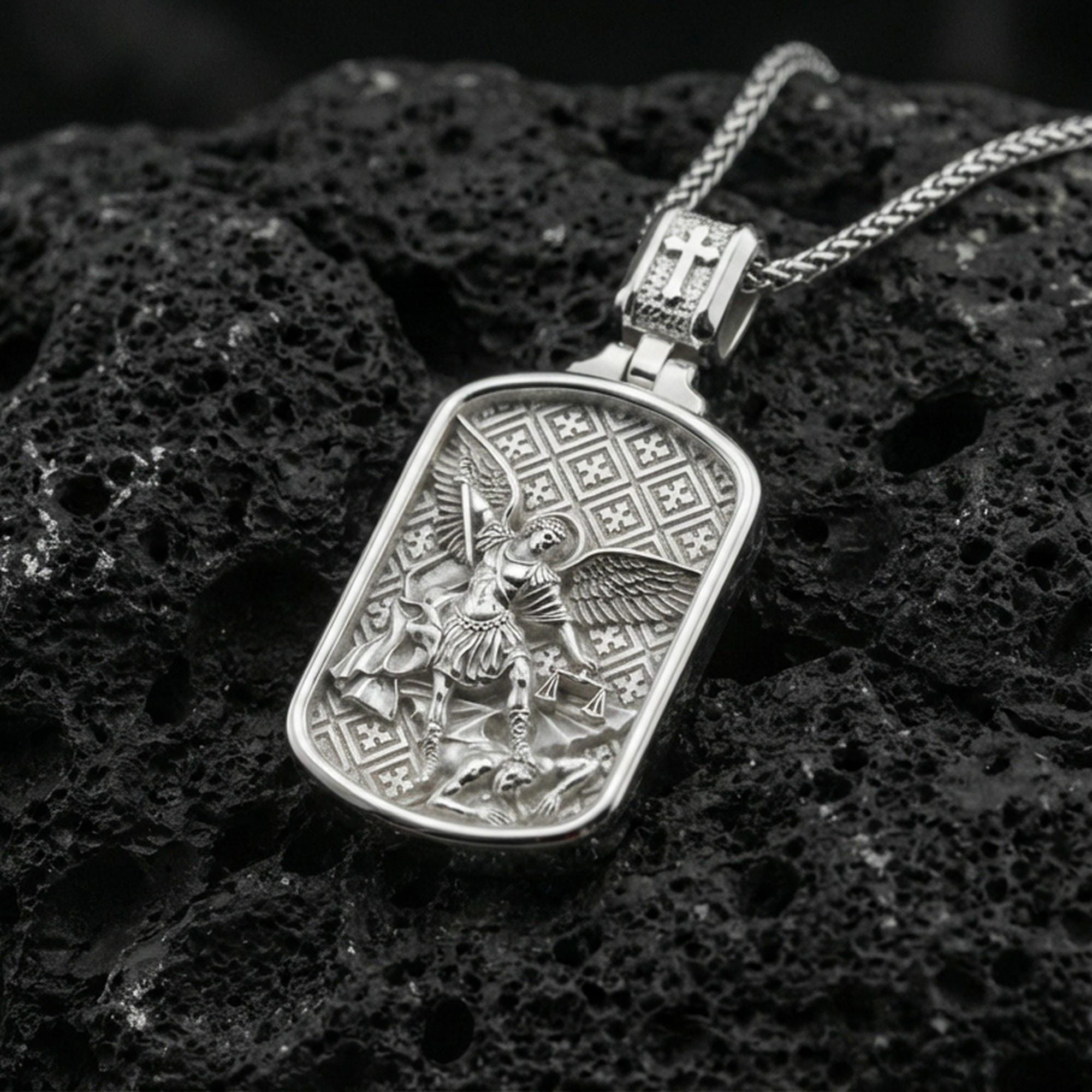 Polished silver Archangel Michael dogtag necklace pendant on black volcanic stone background, crisp rectangular frame and patterned backdrop, high-end product shot