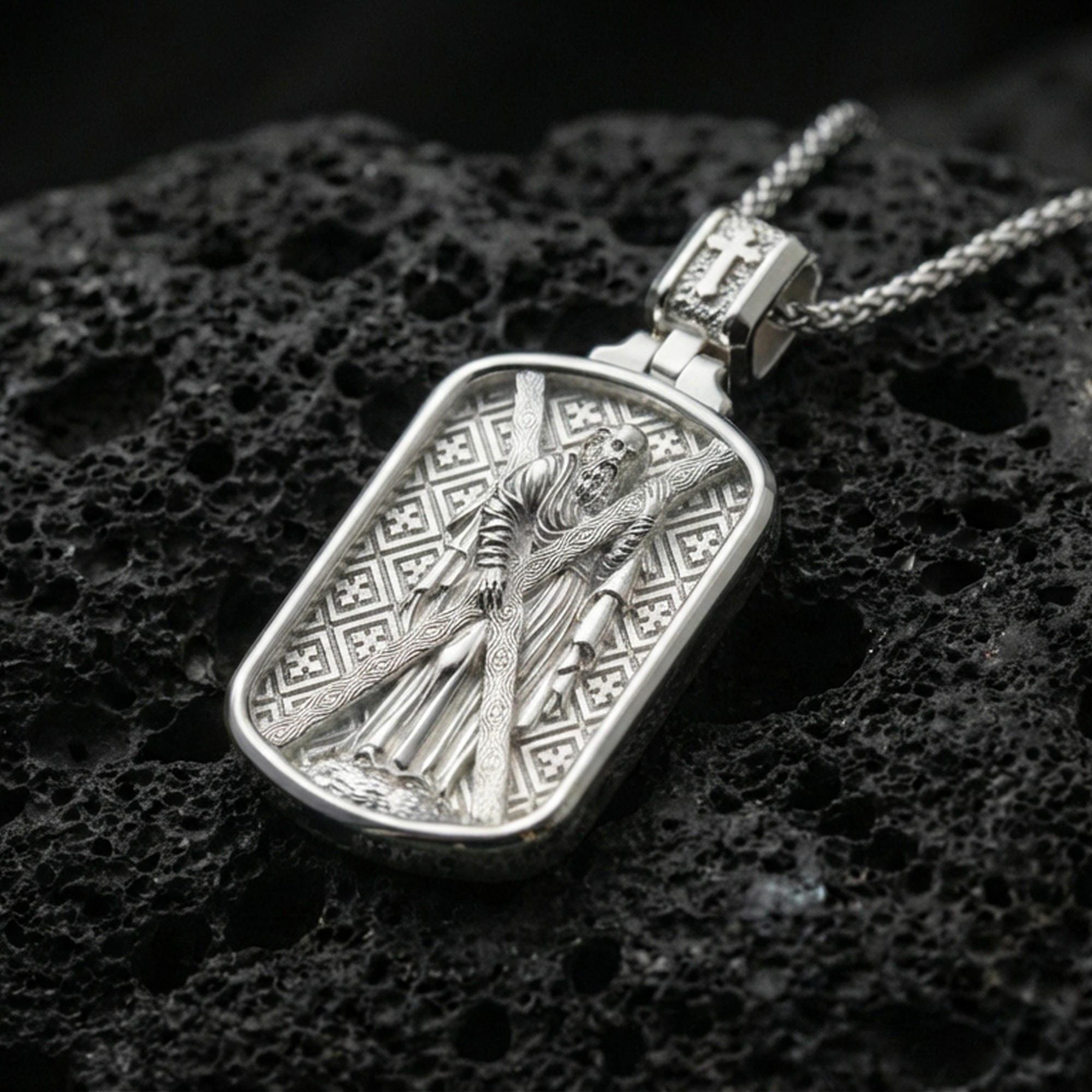 Polished silver Saint Andrew dogtag pendant necklace on black volcanic stone, crisp rectangular frame and patterned background, high-end product photo
