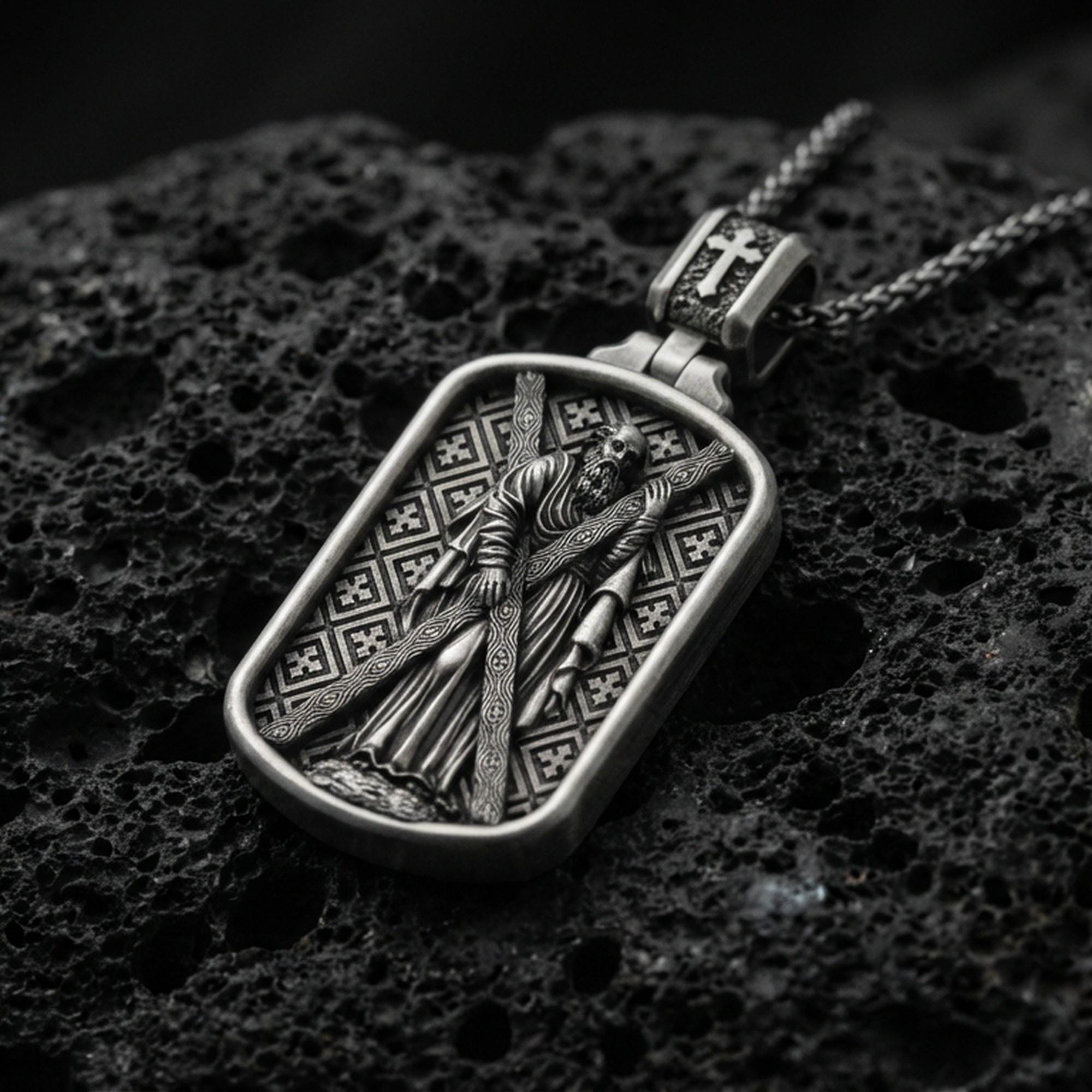 Oxidized Saint Andrew dog tag pendant on volcanic rock, macro close-up, apostle holding cross relief, premium studio lighting