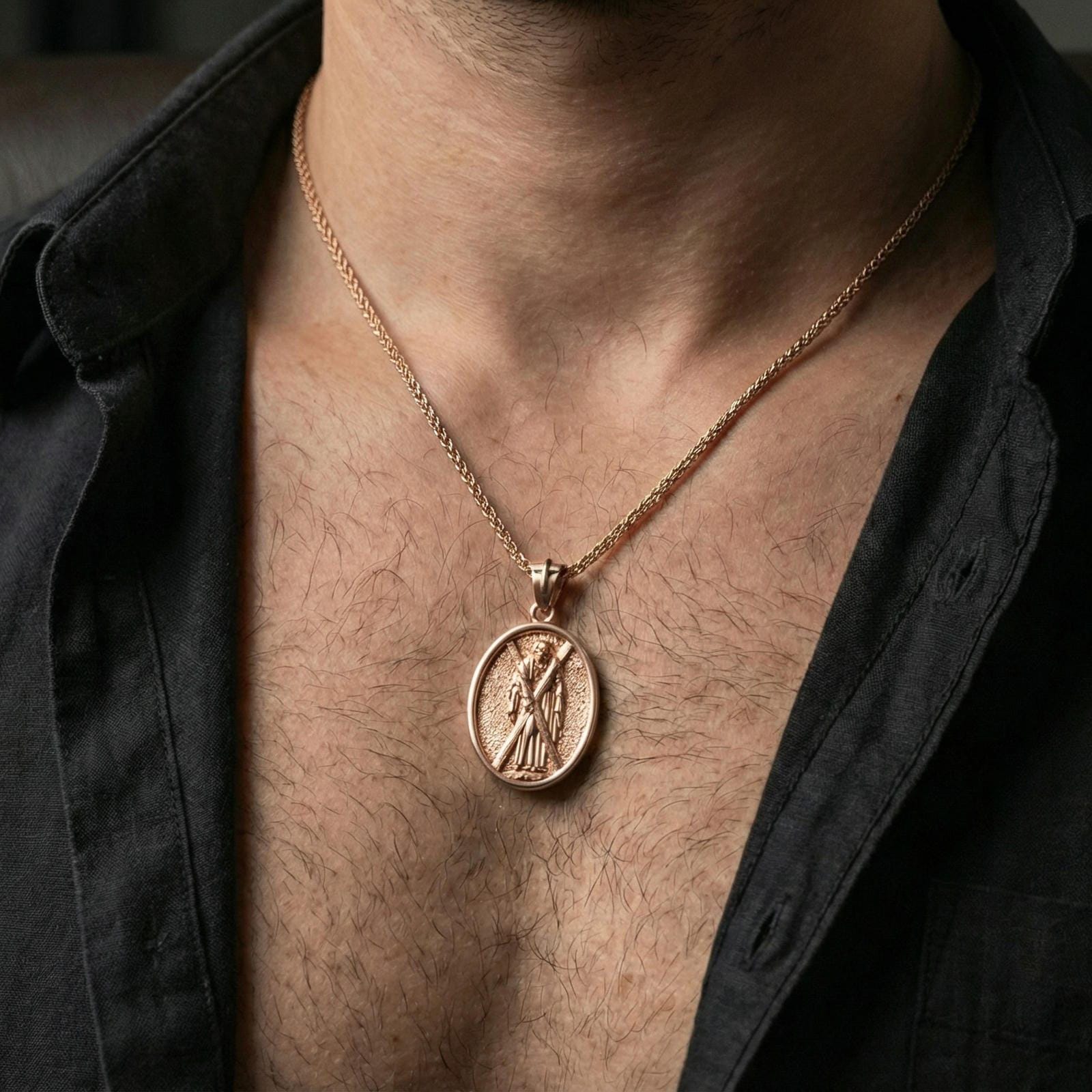 Rose gold plated Saint Andrew oval medallion pendant necklace worn on neck, dark clothing lifestyle shot, oval pendant in sharp focus