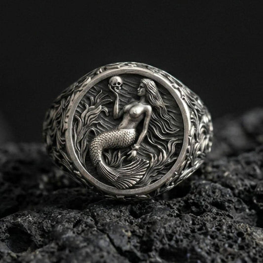 Oxidized mermaid ring on volcanic rock, fantasy ocean scene with mermaid and skull detail, ornate engraved band, macro close-up