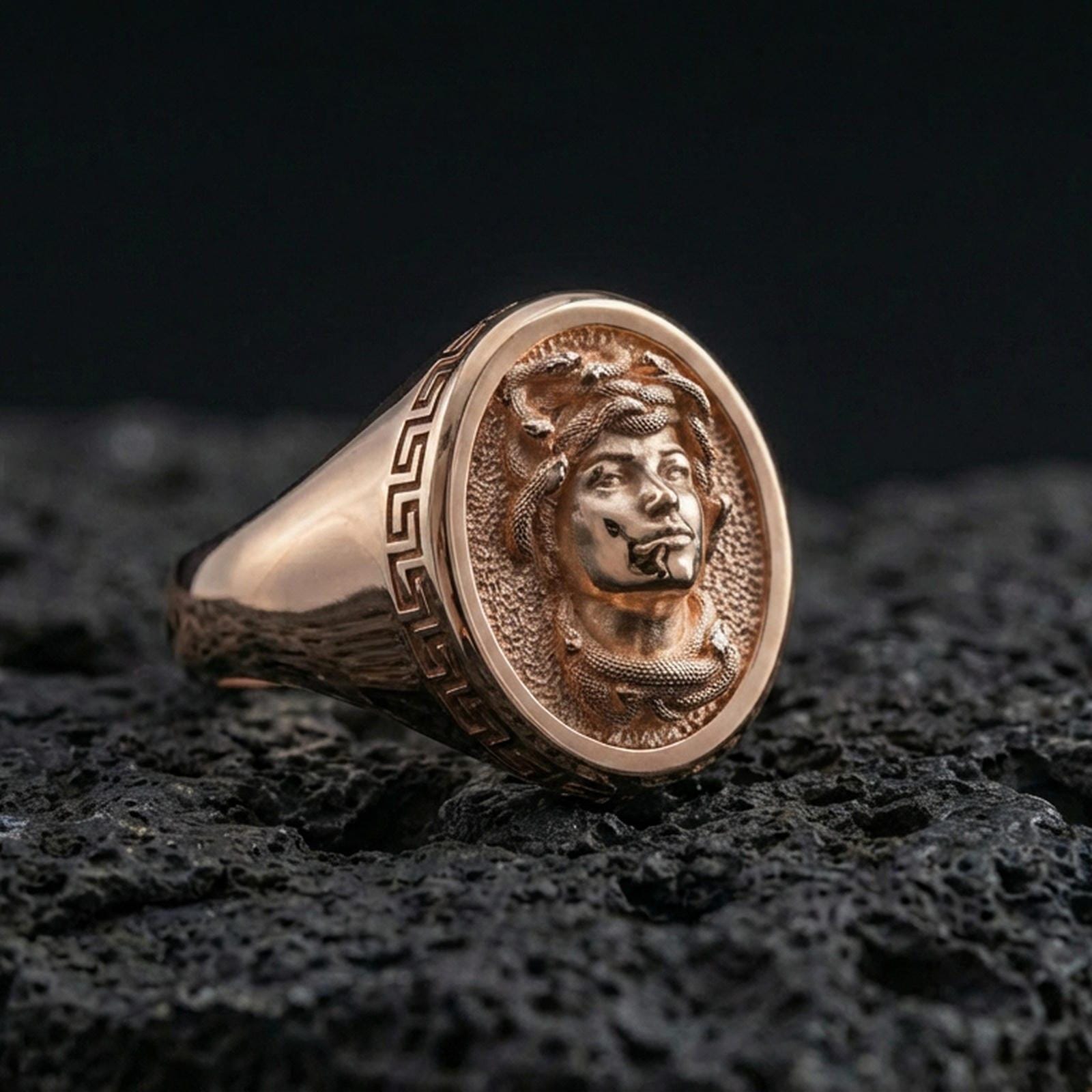 Rose gold plated Medusa ring featuring gorgon head relief and Greek key frame on volcanic rock backdrop