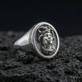 Load image into Gallery viewer, Polished silver Medusa ring close-up showing detailed gorgon portrait and classic Greek key edge on volcanic rock
