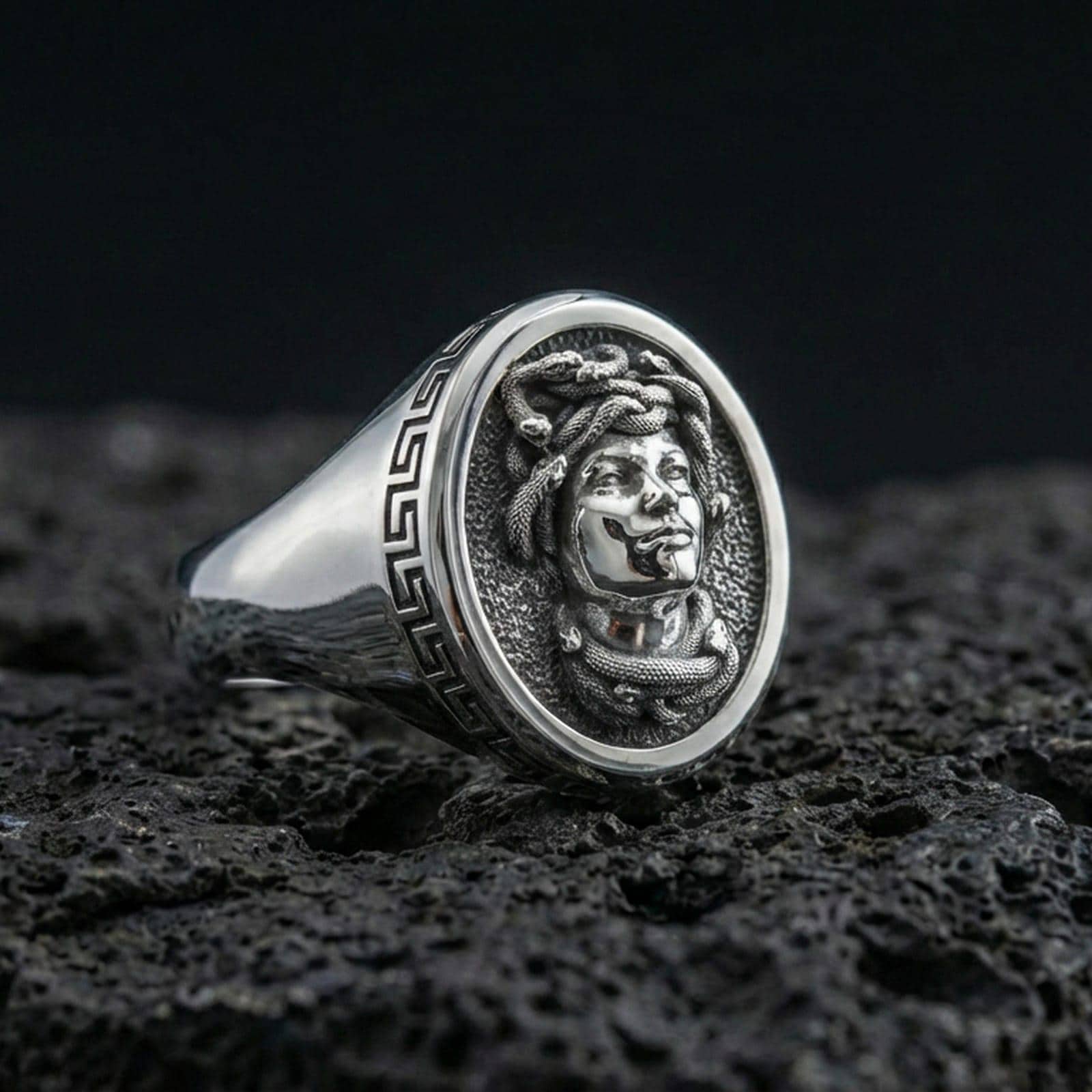 Polished silver Medusa ring close-up showing detailed gorgon portrait and classic Greek key edge on volcanic rock