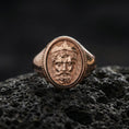 Load image into Gallery viewer, Rose gold plated Poseidon ring on volcanic rock surface, Neptune/Poseidon portrait engraving, classic Greek pattern accents, luxury lighting
