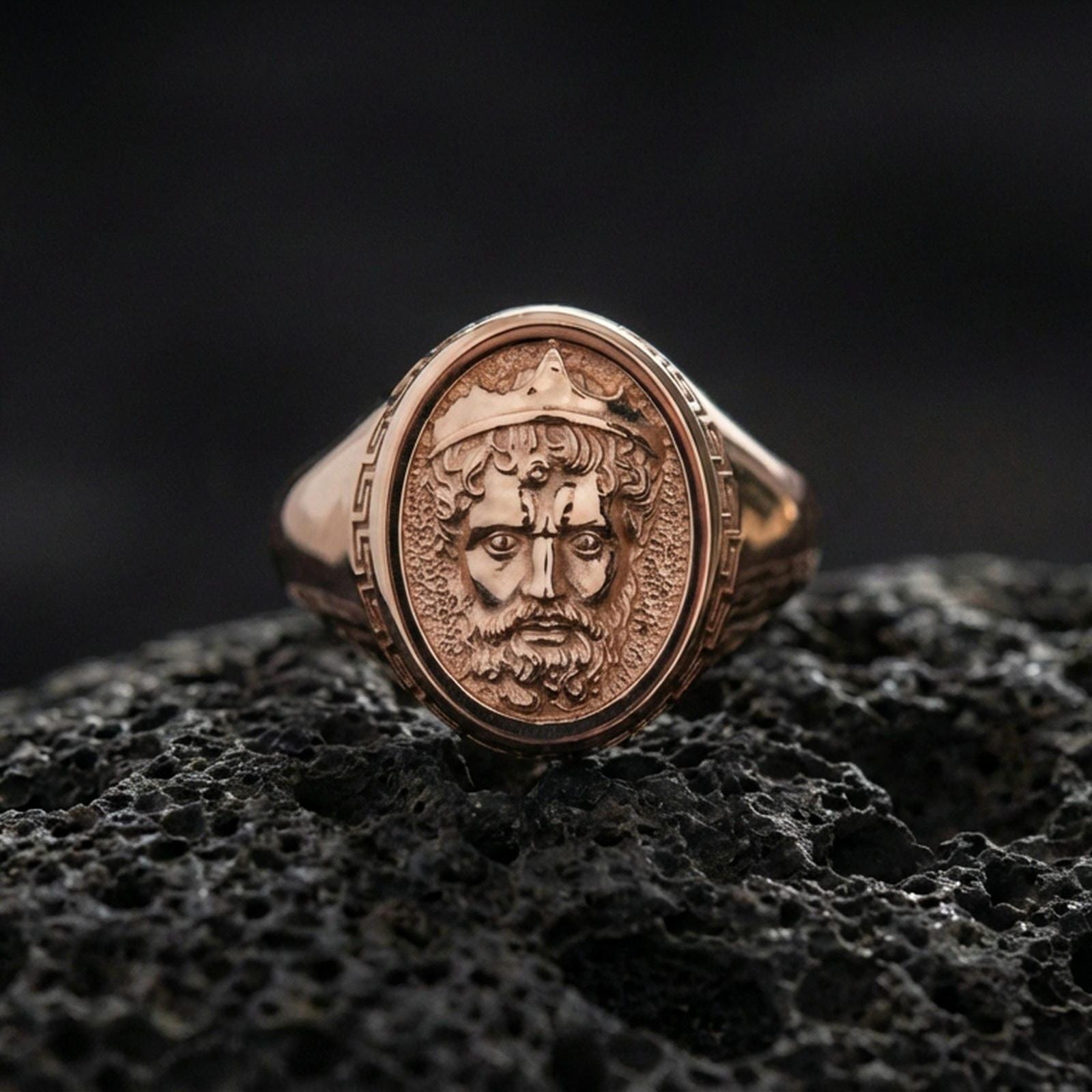 Rose gold plated Poseidon ring on volcanic rock surface, Neptune/Poseidon portrait engraving, classic Greek pattern accents, luxury lighting