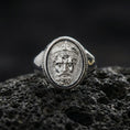 Load image into Gallery viewer, Polished silver Poseidon signet ring on black volcanic stone, Neptune-inspired crowned face relief, Greek key side detail, close-up
