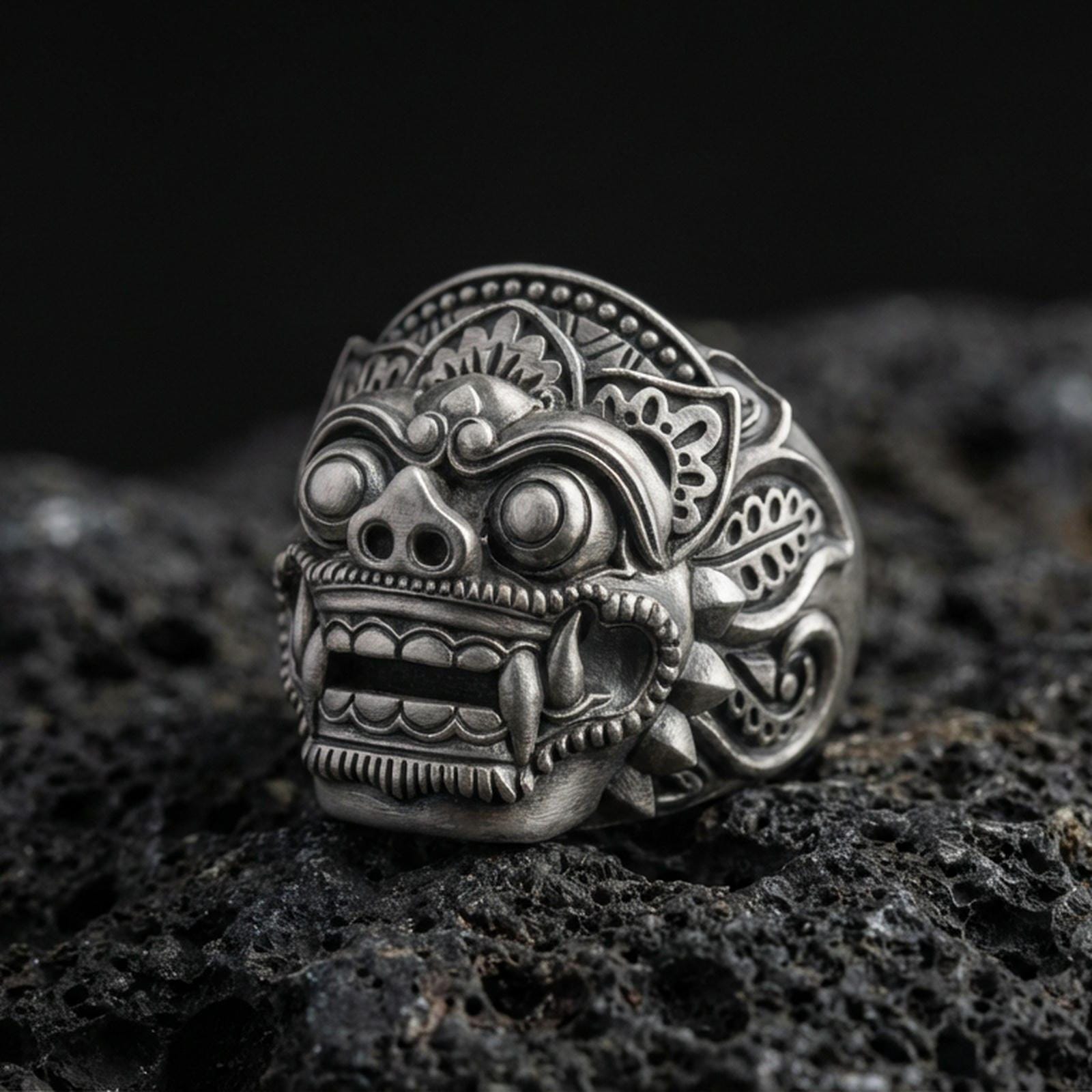 Balinese Barong god sterling silver ring in an oxidized finish on volcanic rock, macro studio product photo