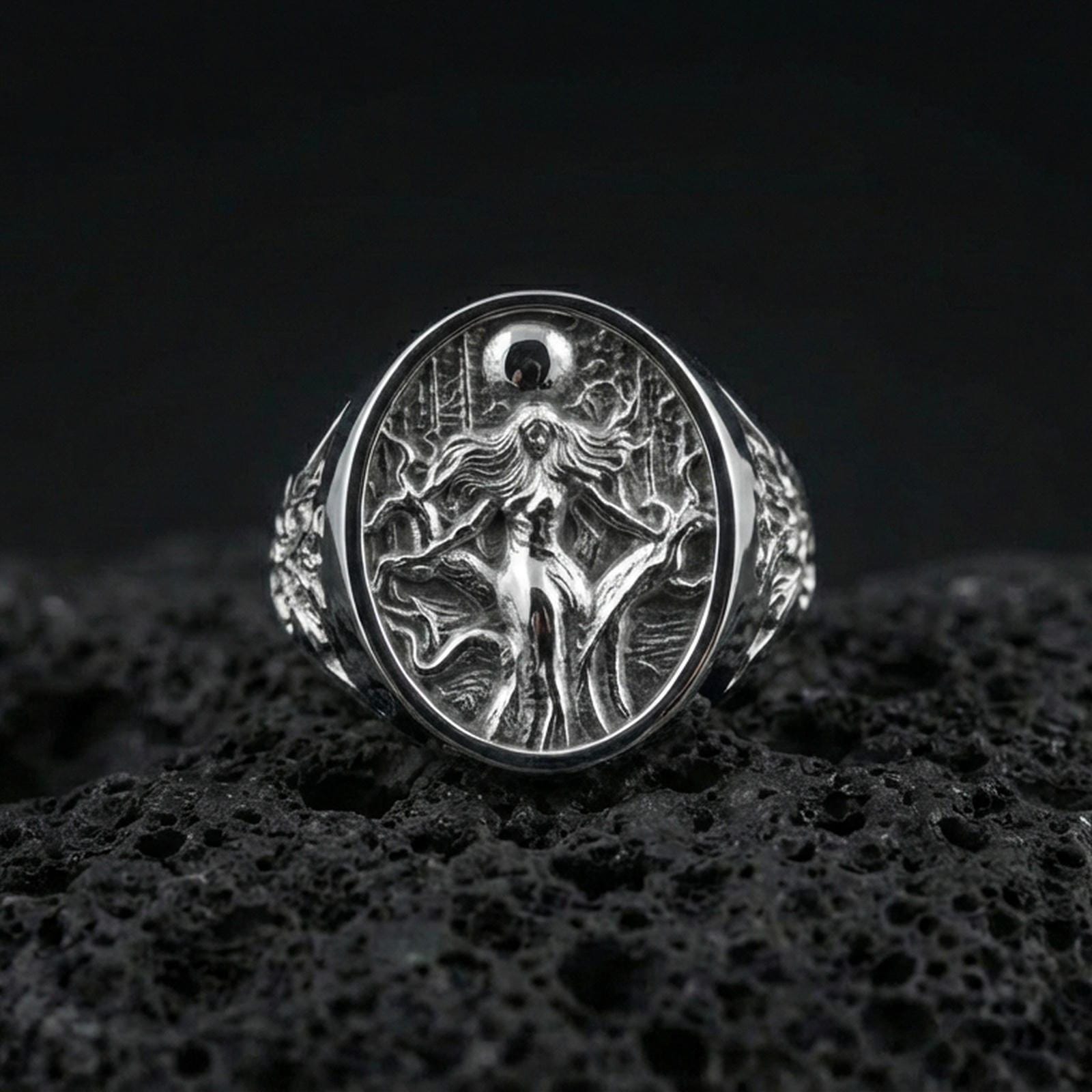 Sterling silver Freya ring in polished silver finish on volcanic rock, detailed Norse mythology goddess relief, close-up photo