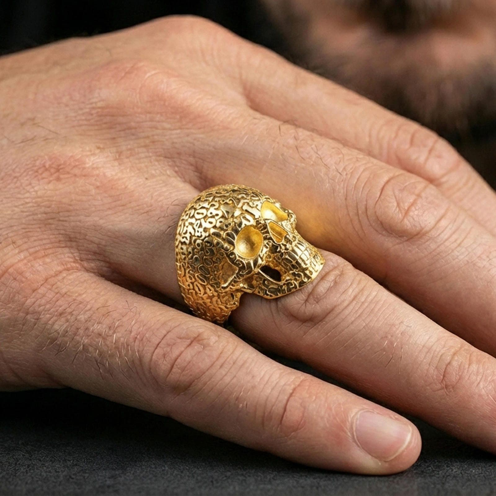 Skull numerology signet ring in a gold plated finish worn on finger, statement memento mori design with engraved numbers, masculine lifestyle close-up