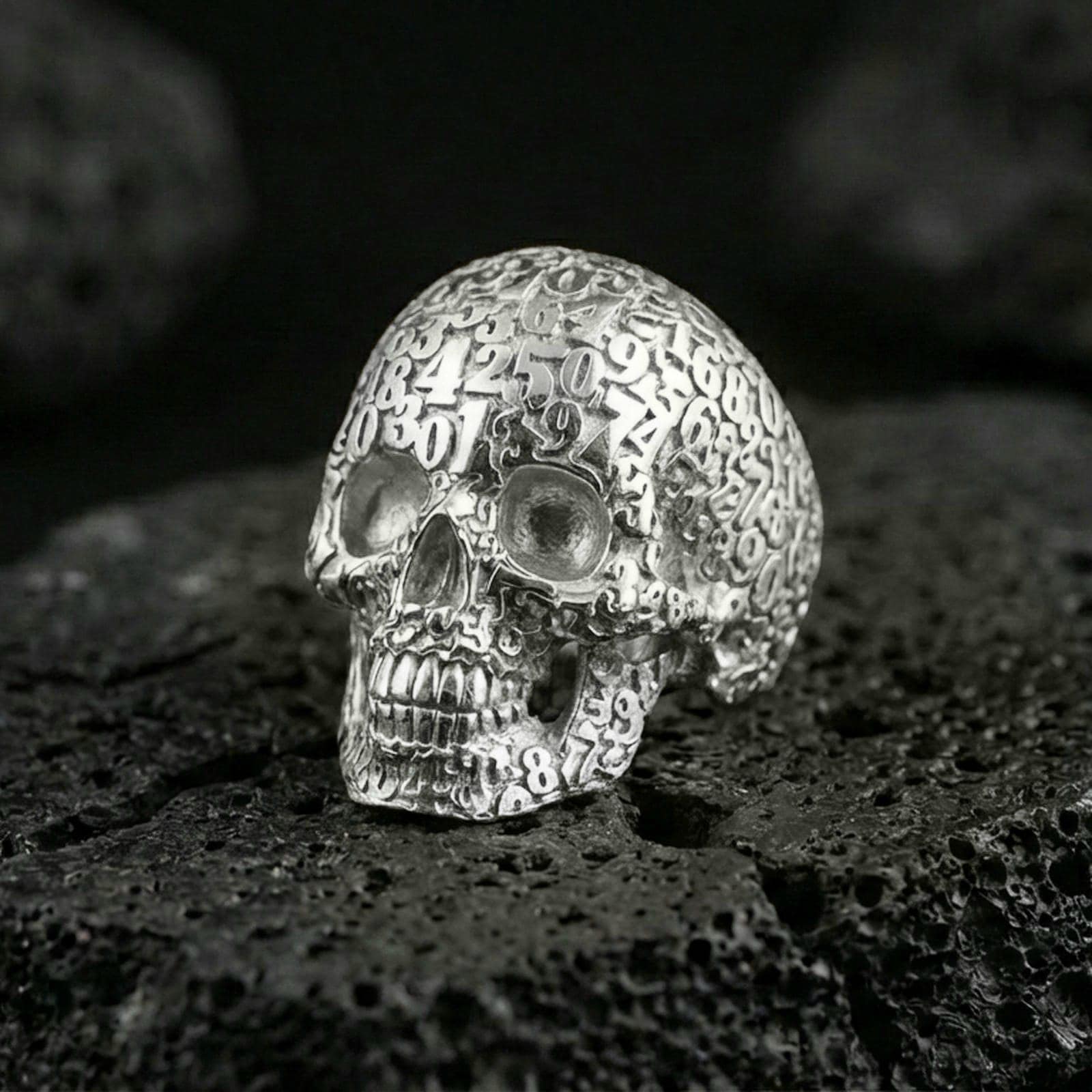 925 sterling silver skull ring in polished silver finish on volcanic rock, raised numbers and detailed teeth carving, close-up product photo