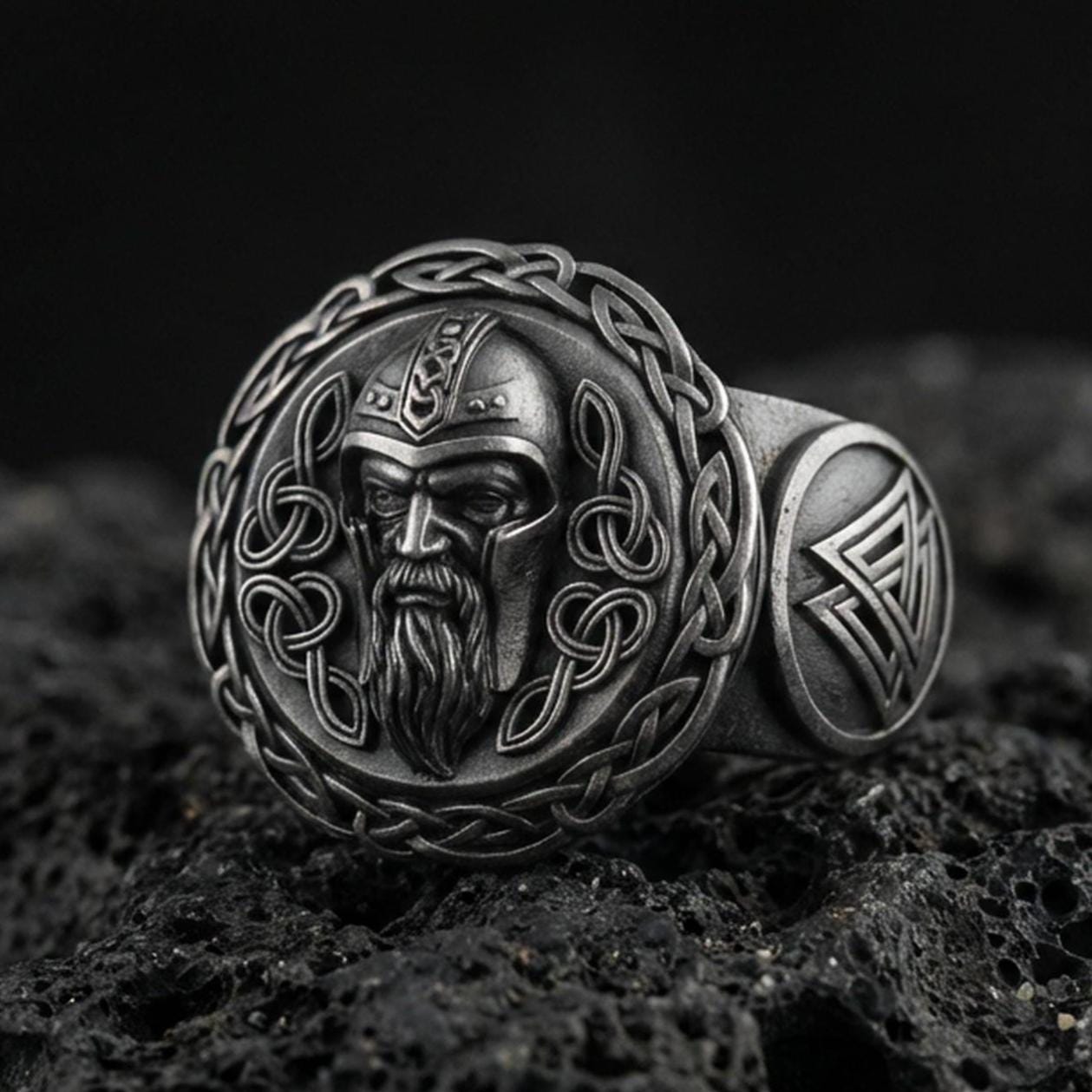 Odin the All-Father sterling silver ring in an oxidized finish on volcanic rock, Viking warrior portrait with Celtic knot border, macro studio product shot